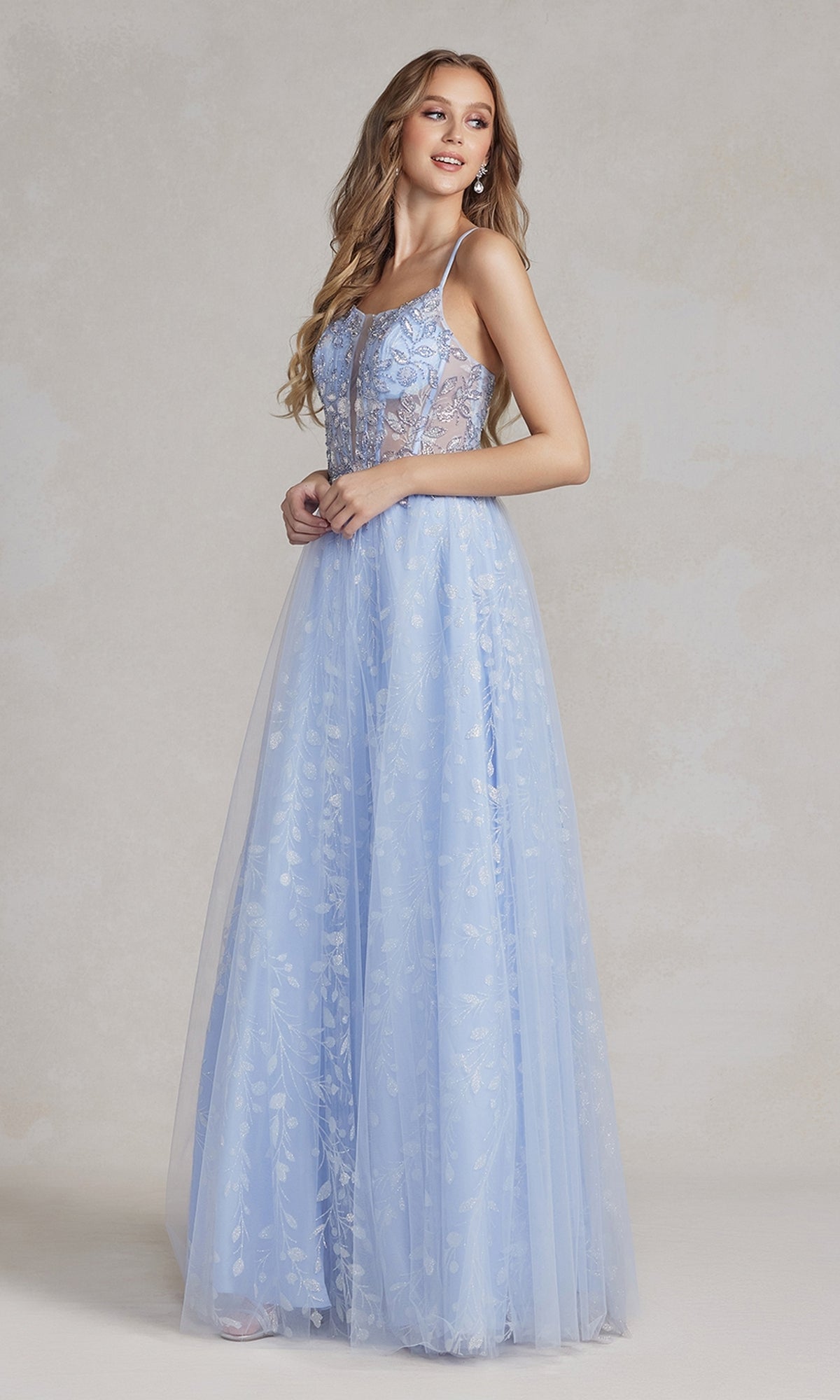 A woman wearing the Periwinkle Illusion-Bodice Long Prom Dress with floral embroidery and thin straps stands against a neutral background.