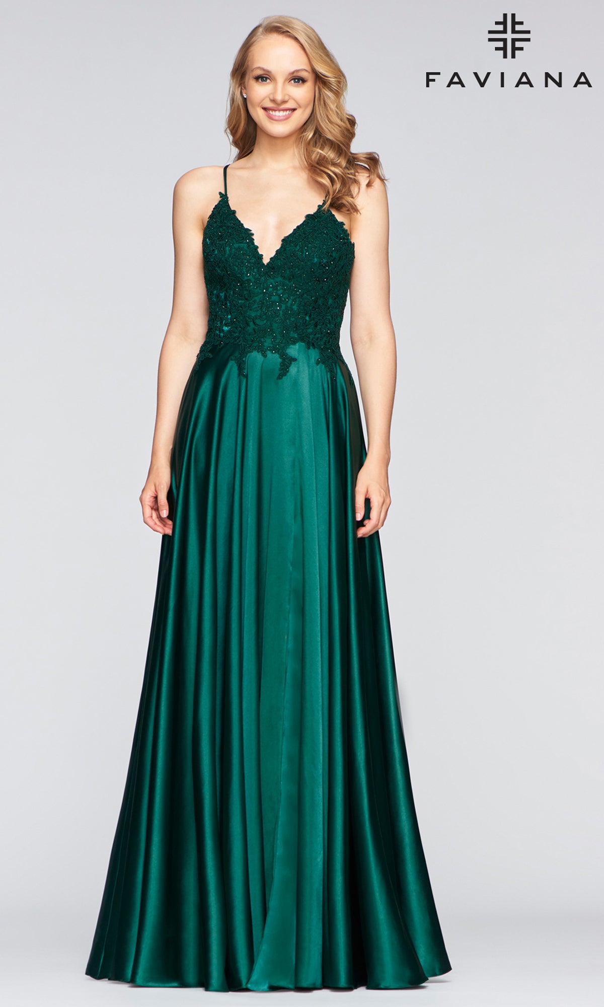 A woman models the Faviana Lace-Bodice Long A-Line Prom Dress, featuring an emerald green embroidered lace bodice and flowing satin skirt, standing before a plain backdrop with the Faviana logo.
