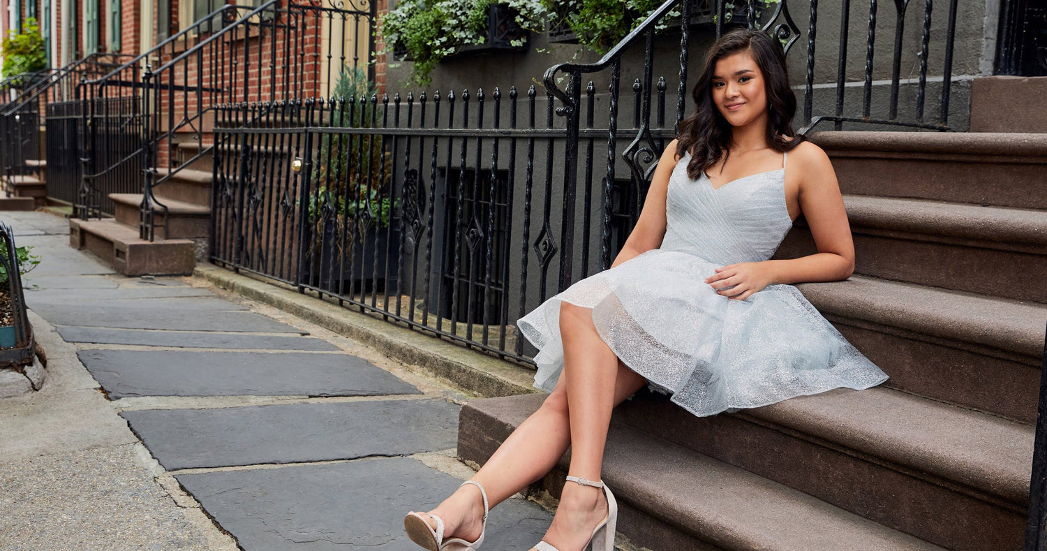 Teen girl in a white graduation party dress sitting on steps off a city sidewalk.