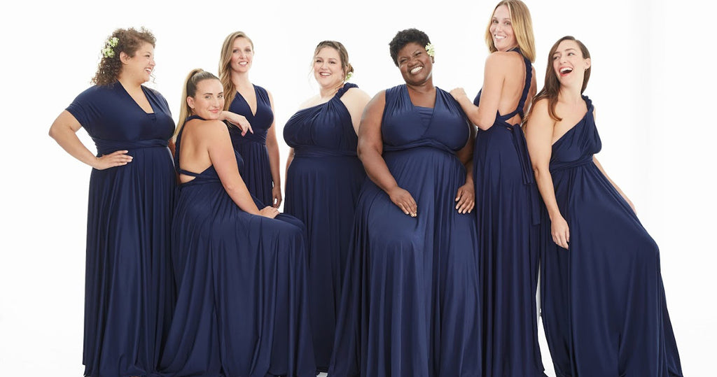 Group of seven women wearing the same navy blue convertible bridesmaid dress styled differently for each woman.