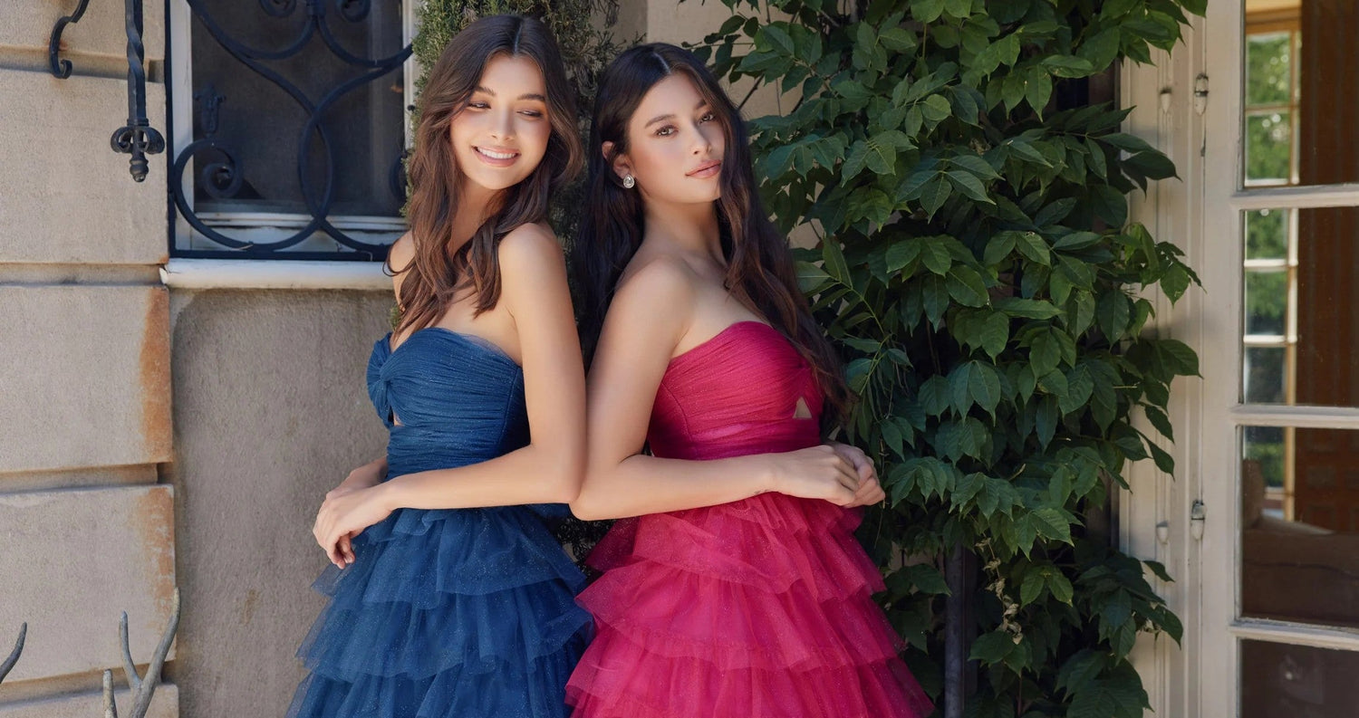 Image of two women standing outside modeling the same short homecoming dress with ruffles in two different colors. One is a dark midnight blue homecoming dress and the other is a rose pink homecoming dress.