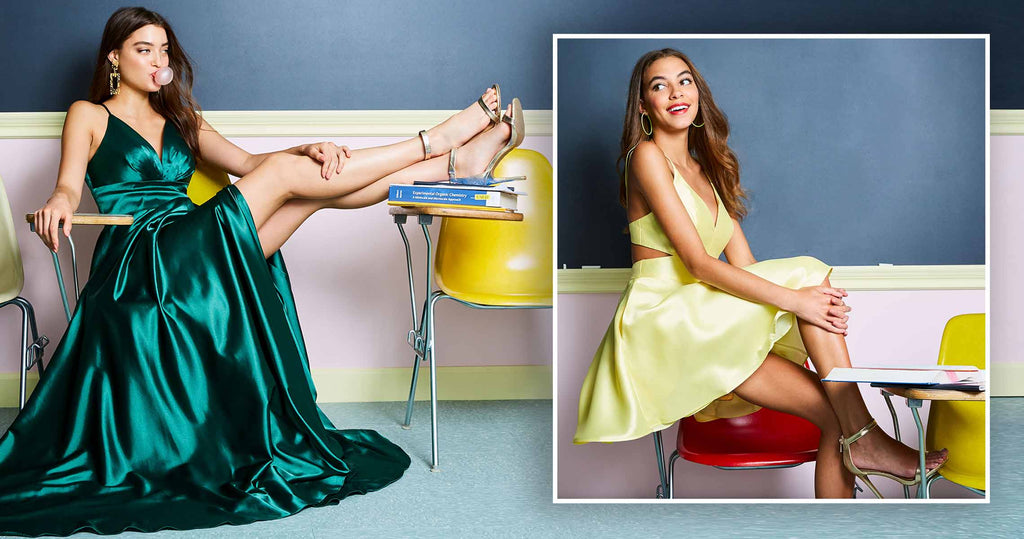 Two teen girls in a classroom, one wearing a green prom dress, the other wearing a yellow homecoming dress.