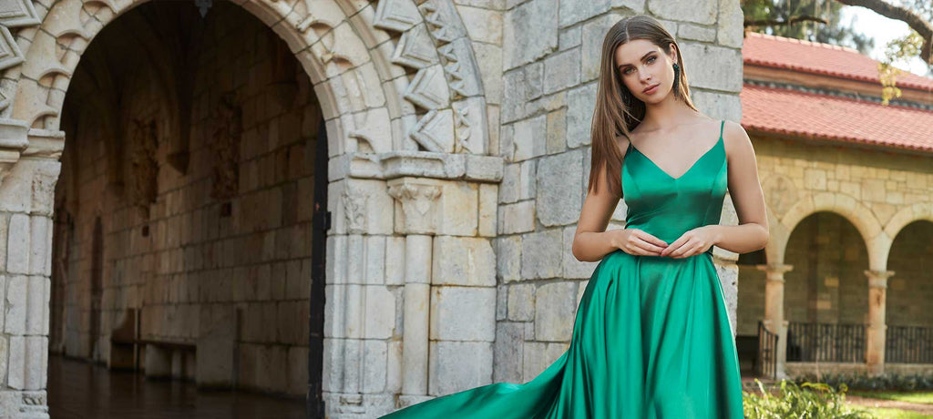 Teen girl wearing a green prom dress in front of a stone archway.