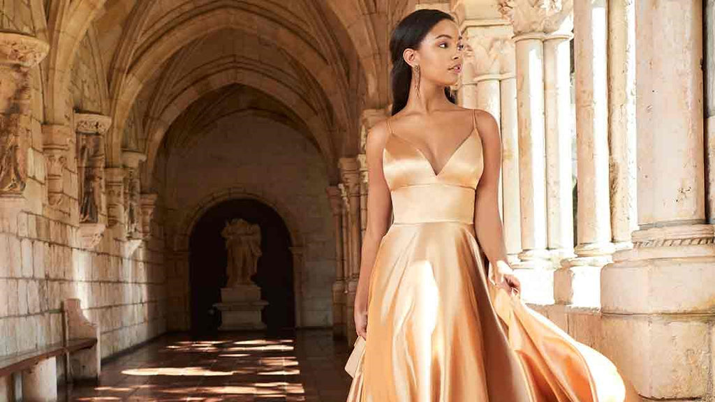 Teen girl wearing a gold v-neck prom dress in a castle-esque building.