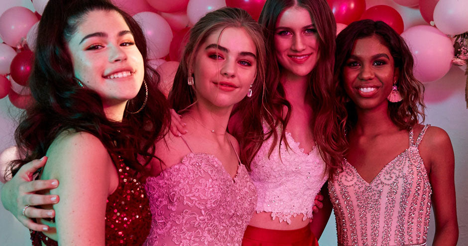 Close up of four teens wearing embroidered dresses in front of a balloon backdrop.