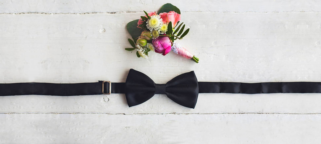 A colorful flower corsage next to a black bow tie.