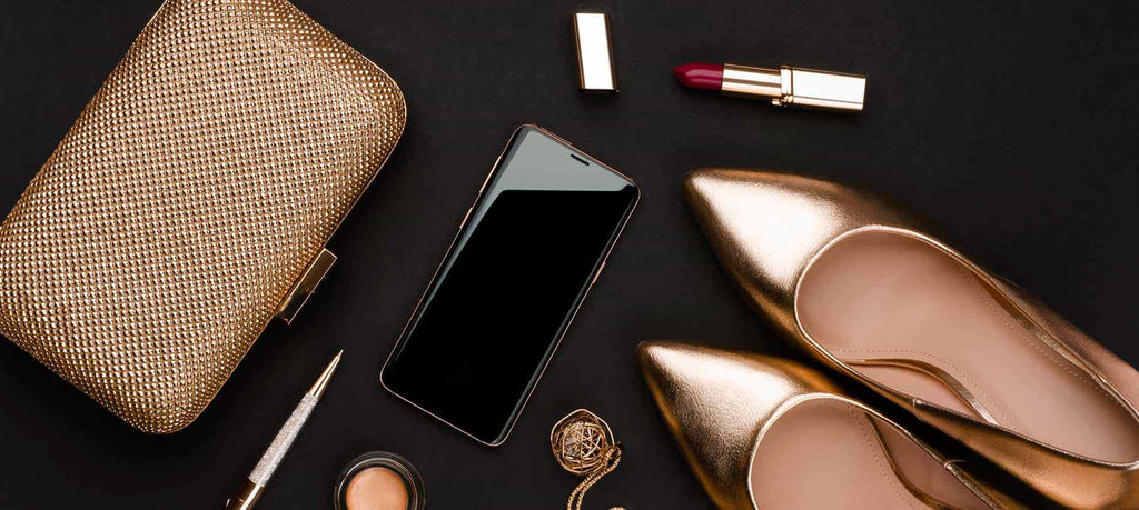 Prom essentials, including a gold clutch, pen, cell phone, foundation, lipstick, gold necklace, and gold prom shoes.