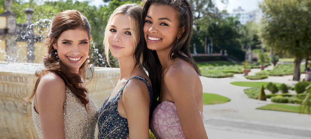 Close up of three teen girls wearing prom dresses and smiling in front of a garden fountain.