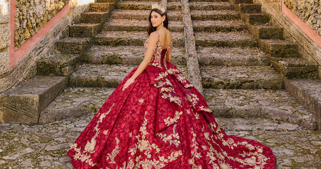 Teen girl wearing a red lace quince ball gown with gold floral embroidery and a crown.