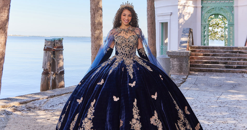 Teen girl wearing a navy blue quince ball gown, matching elbow gloves, and a matching sheer cape.