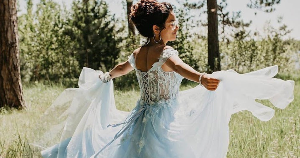Teen girl twirling in the woods in a pale blue sheer prom dress with lace-up corset back.