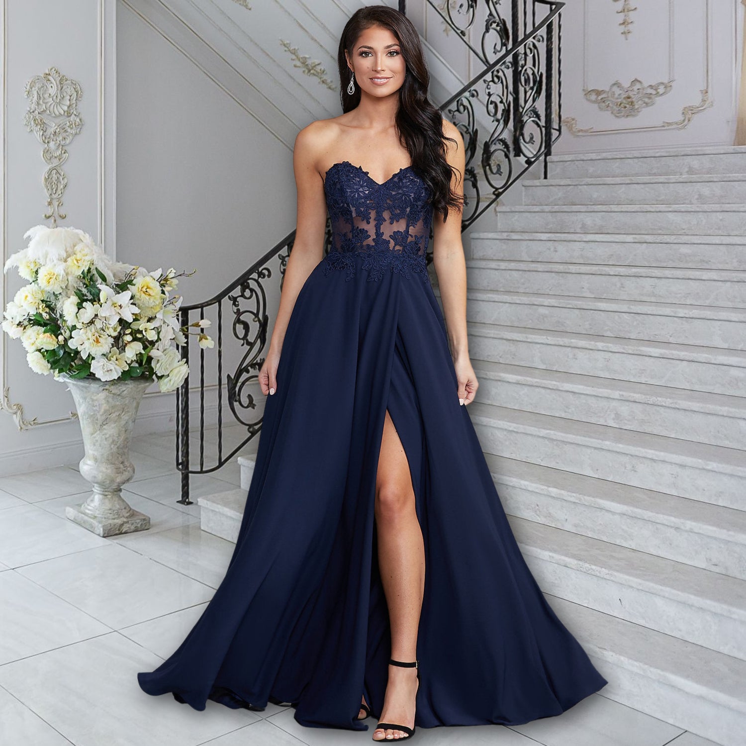 Image of a woman standing at the bottom of a staircase in a ball room wearing a long a-line dark blue dress.