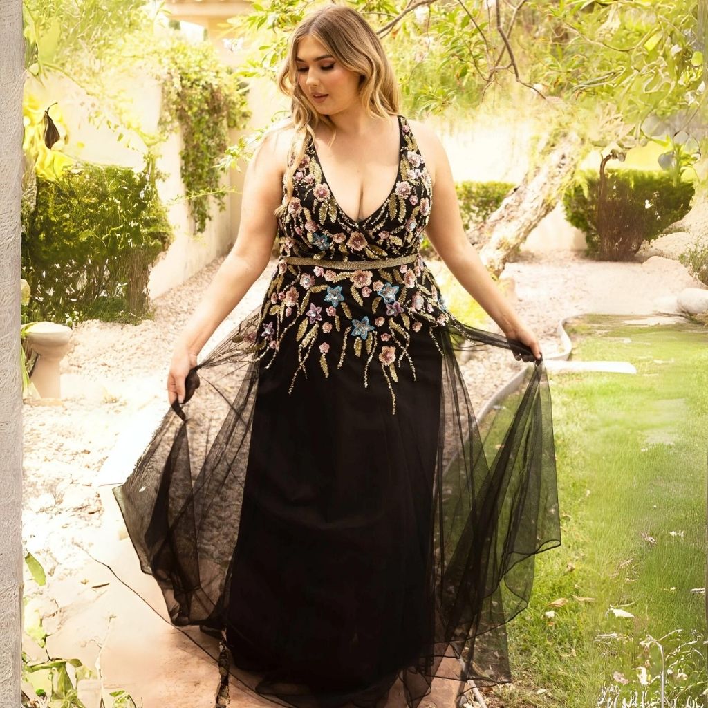 Holding out the tulle skirt of her plus-size floral-print black formal dress, a woman stands an a stone garden path.