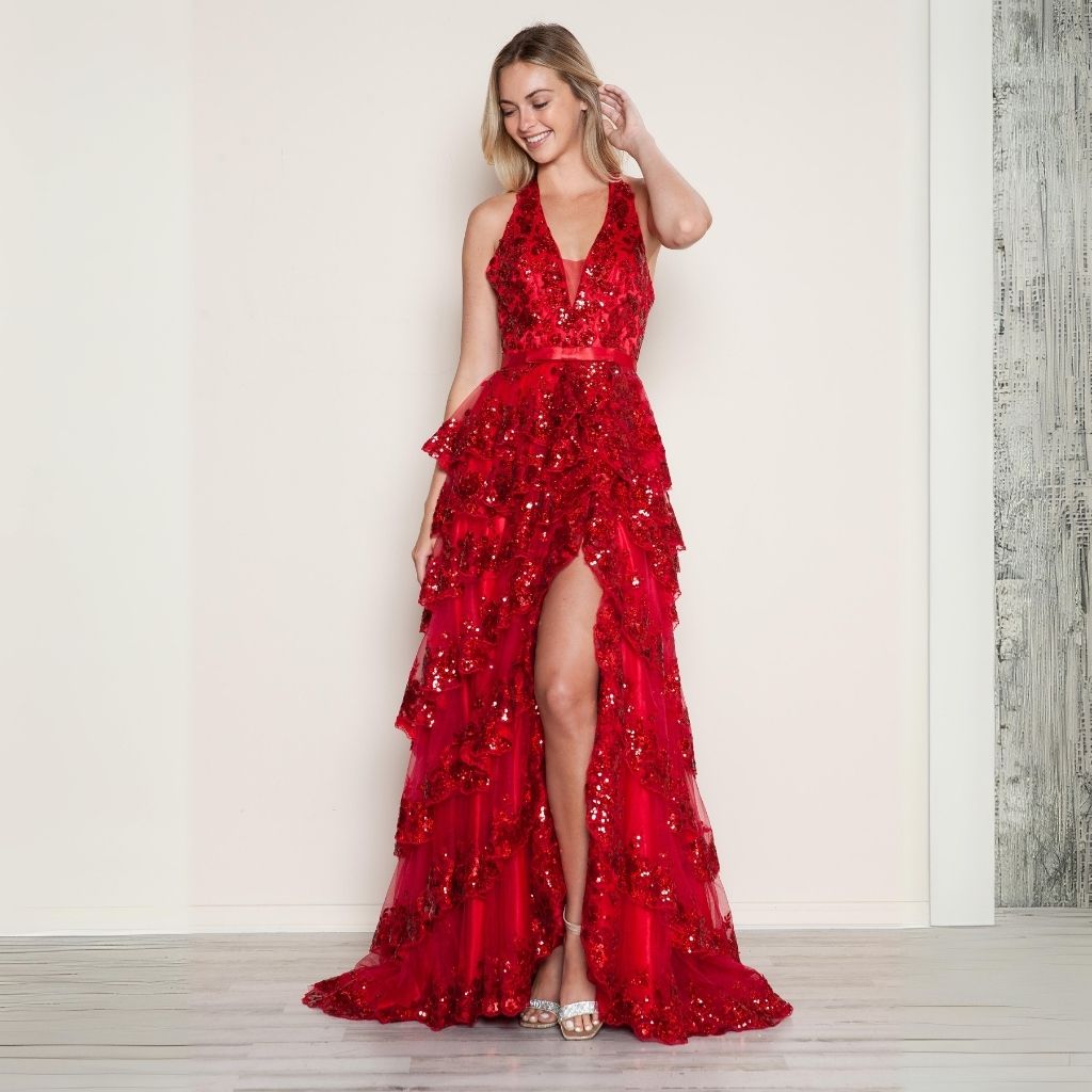 In a red sequin tiered prom dress by Poly USA, a teen girl poses in front of a white wall.