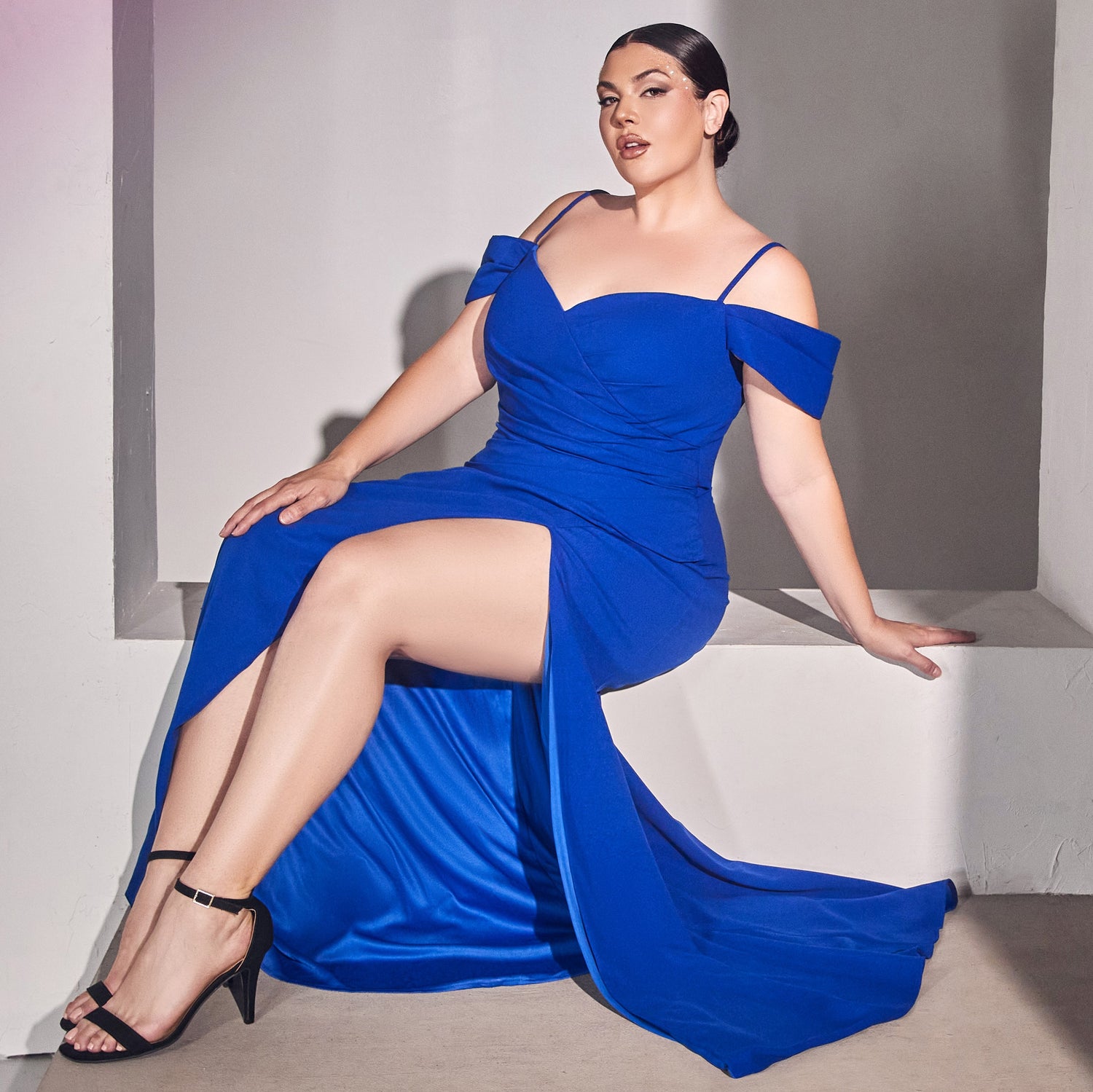 Image of woman sitting down wearing a long royal blue plus-size prom dress.