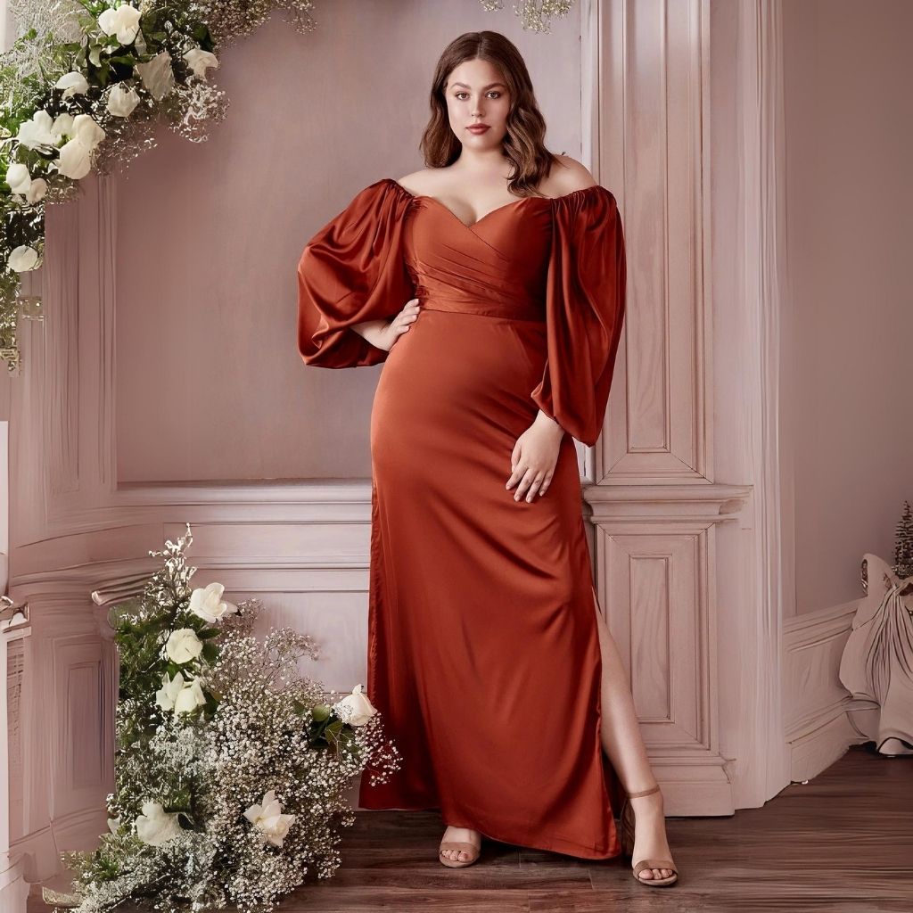 In an off-the-shoulder plus-size formal dress with flared sleeves, a woman stands next to white flower arrangements.