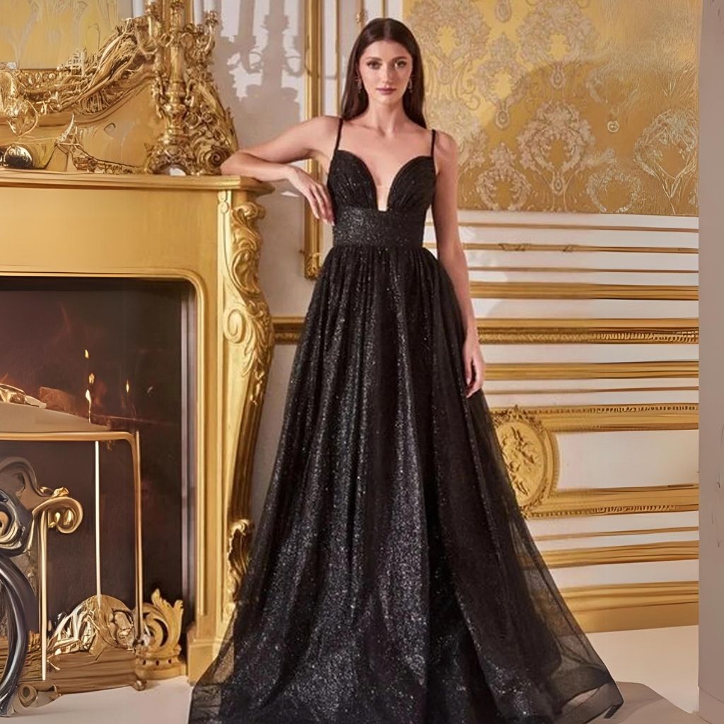 In a black glitter empire-waist formal dress, a woman leans against a golden fireplace in front of a golden wall.