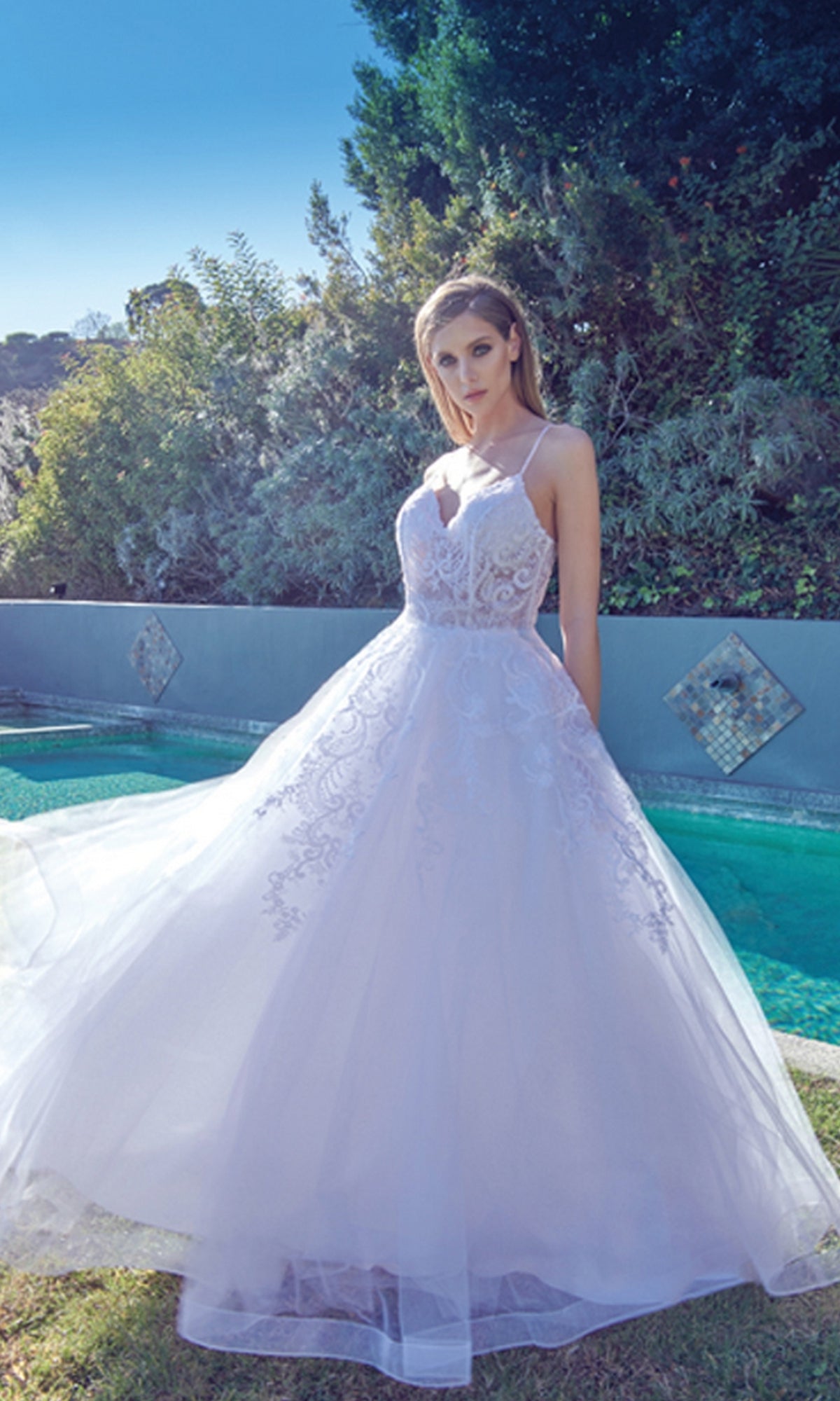A woman in the Embroidered Glitter-Tulle Long Prom Ball Gown 251 poses outdoors by a pool amid lush greenery and a tiled wall.