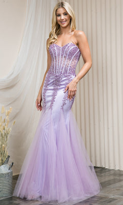 A woman in the Sheer-Corset Strapless Mermaid Prom Dress 774, featuring a jeweled corset bodice, sheer panels, and decorative beading, stands indoors on a wooden floor.