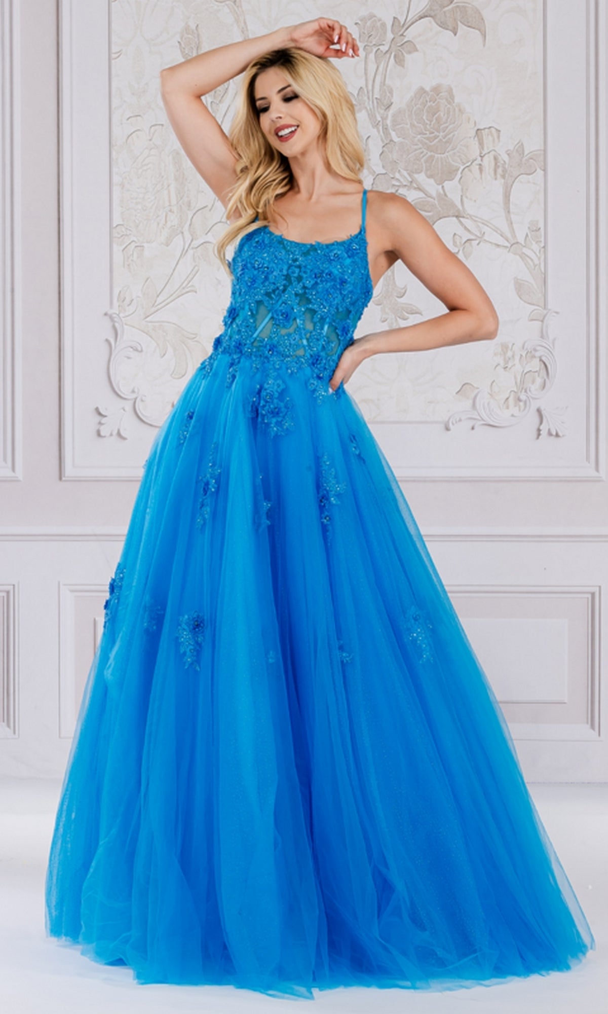 A woman models the Embroidered-Tulle Long A-Line Prom Ball Gown 7035, a floor-length, bright blue dress with floral embroidery and a tulle skirt, set against an ornate, light background.