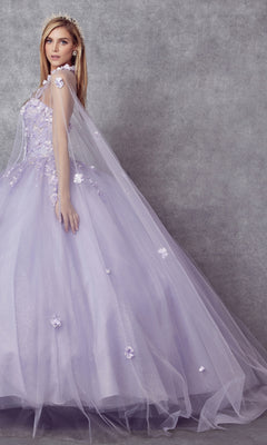A woman wearing the Juliet 1435 Strapless Ball Gown Quinceañera Dress, featuring lavender floral appliqués and a sheer cape, stands against a gray textured backdrop.