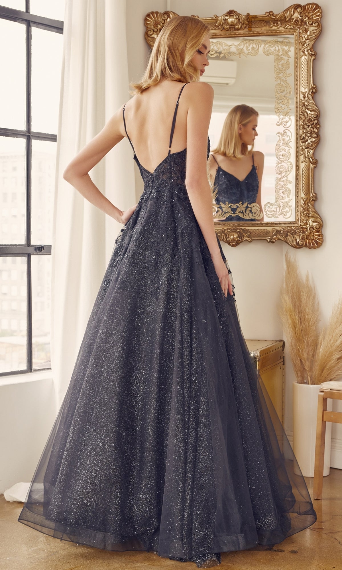A woman wearing the Embroidered Glitter-Tulle Long Prom Ball Gown 251 with thin straps and a backless design stands before a large ornate mirror.