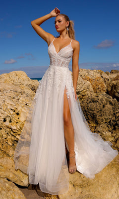 A woman in the Floral-Embroidered Long A-Line Prom Dress TM1006, featuring white lace, tulle, spaghetti straps, a high slit, and floral embroidery, stands on rocky terrain beneath a blue sky.