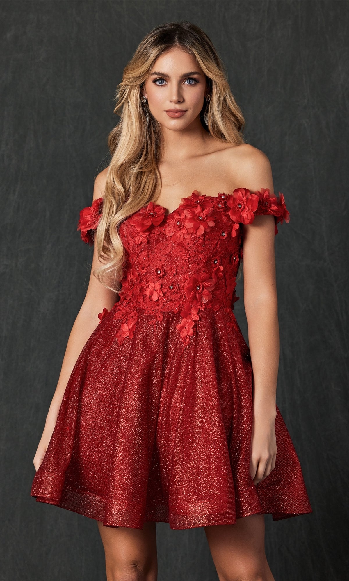 A woman poses against a dark textured background in the Floral Off-the-Shoulder Short Homecoming Dress 861, featuring 3-D flowers and a glittery A-line skirt.