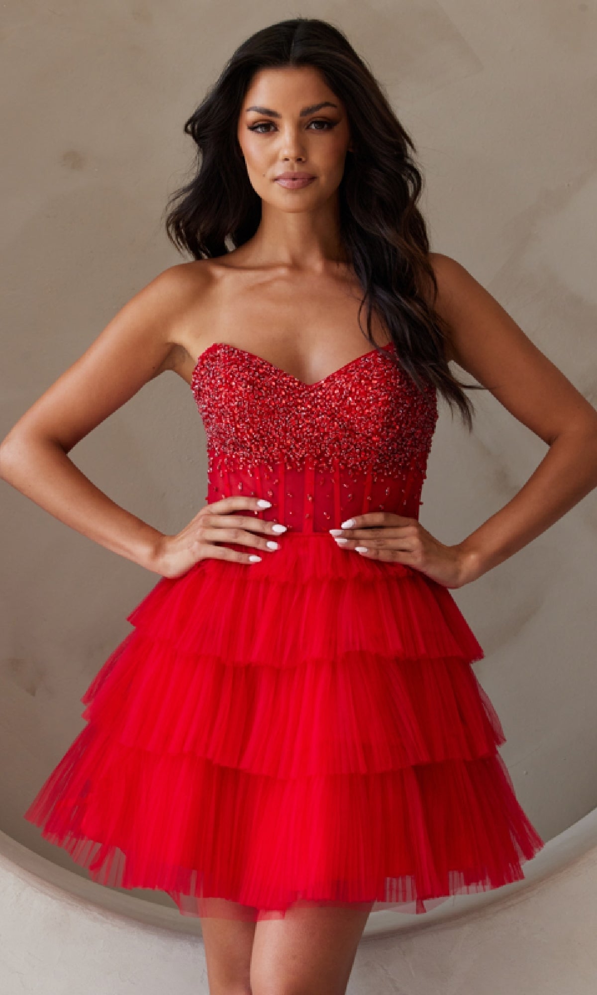 A woman models the Strapless Short Ruffled A-Line Hoco Dress BZ9999S, featuring a beaded bodice and tiered tulle skirt, standing with hands on hips against a neutral background.