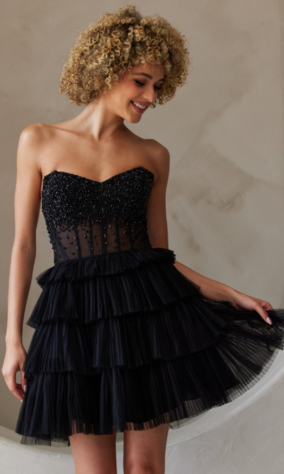 Person wearing the Strapless Short Ruffled A-Line Hoco Dress BZ9999S, featuring a beaded bodice and layered tulle skirt, standing against a neutral textured background.