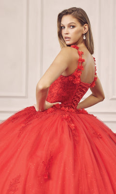 A woman wears the Juliet 1437R Red Ball Gown Quinceañera Dress, featuring floral details and beaded embroidery, as she stands with her back partially turned and looks over her shoulder in front of a white paneled wall.