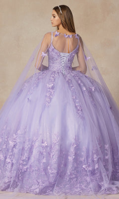 A woman in the Juliet 1442 Quinceañera Dress with Sheer Cape stands facing away, highlighting its elegant lace-up back, floral appliqués, and long, full tulle ball gown skirt.
