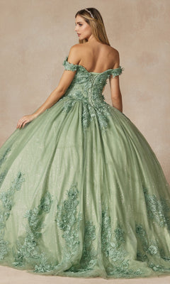 A woman stands gracefully with her back partially turned, wearing the Juliet 1445 Sage Green Quinceañera Dress Ball Gown featuring floral lace, an off-the-shoulder neckline, and a full voluminous skirt.