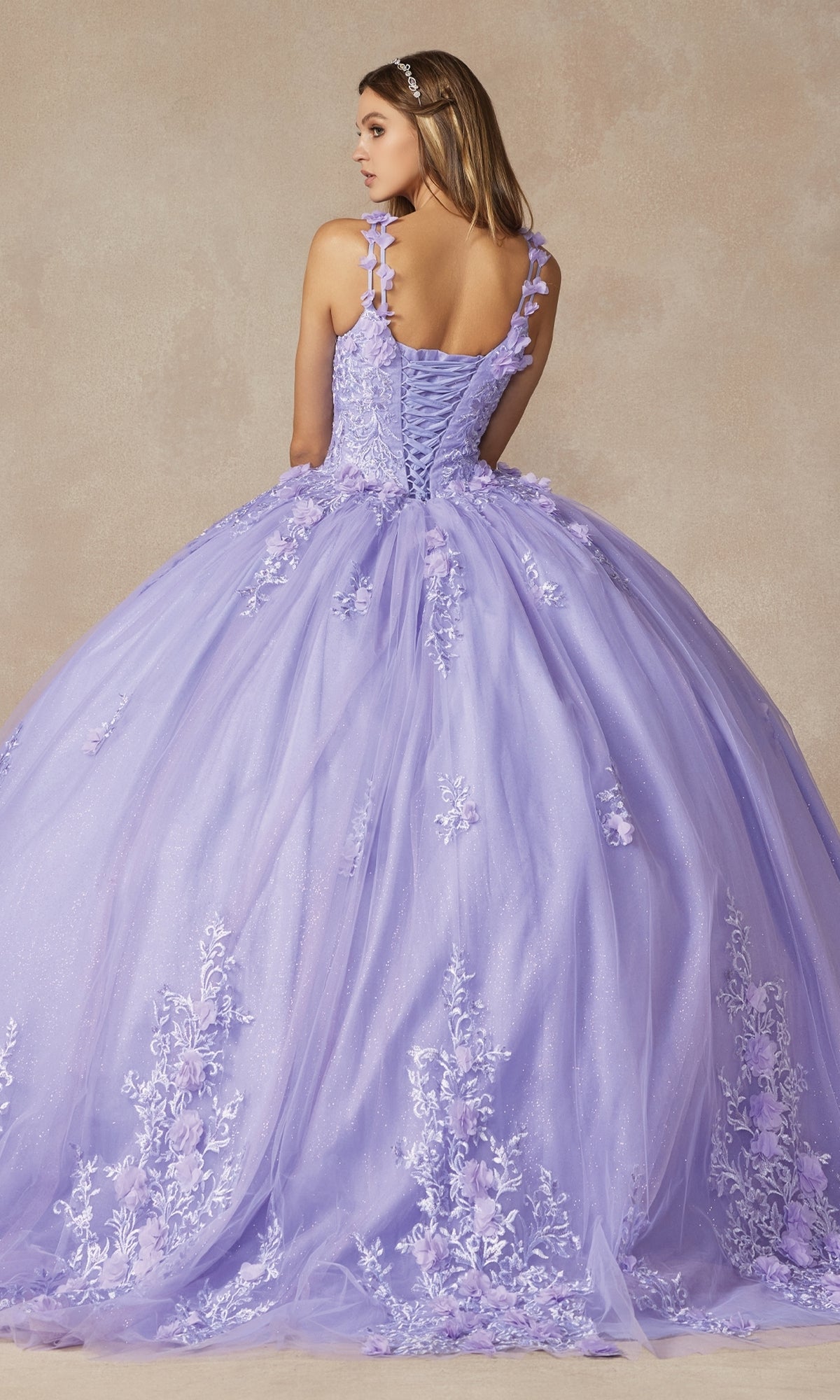 A woman stands with her back to the camera in the Juliet 1437 Lilac Purple Quinceañera Dress, featuring beaded embroidery, floral details, and a lace-up back against a neutral background.
