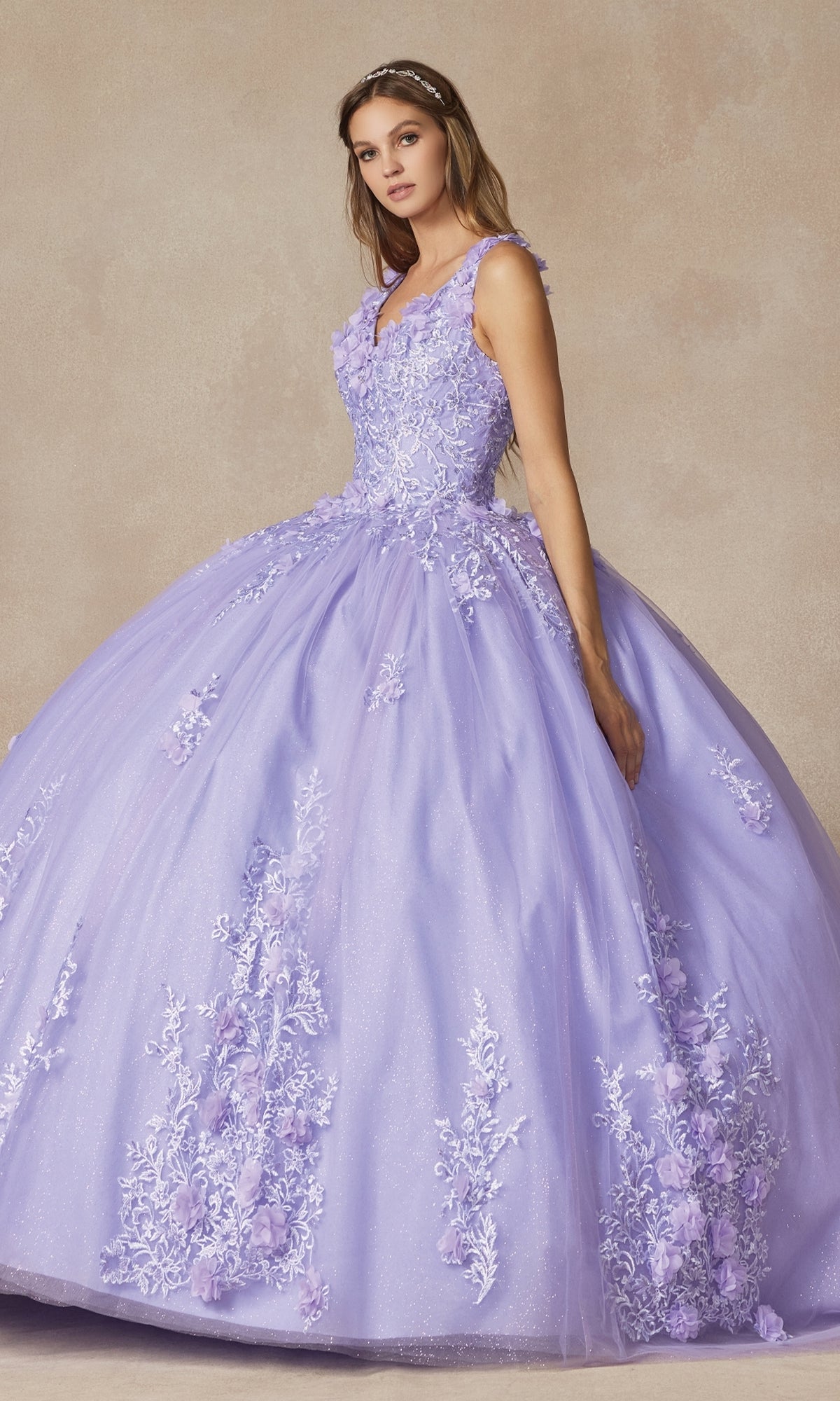 A woman wears the Juliet 1437 Lilac Purple Quinceañera Dress with floral appliques and a full tulle skirt, standing against a neutral background.