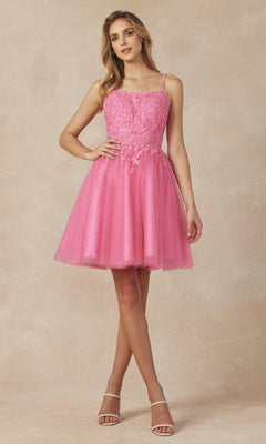 A woman poses against a neutral background in the Embroidered-Corset Babydoll Homecoming Dress 860, featuring a sparkly lace bodice and tulle skirt, paired with strappy nude heels.