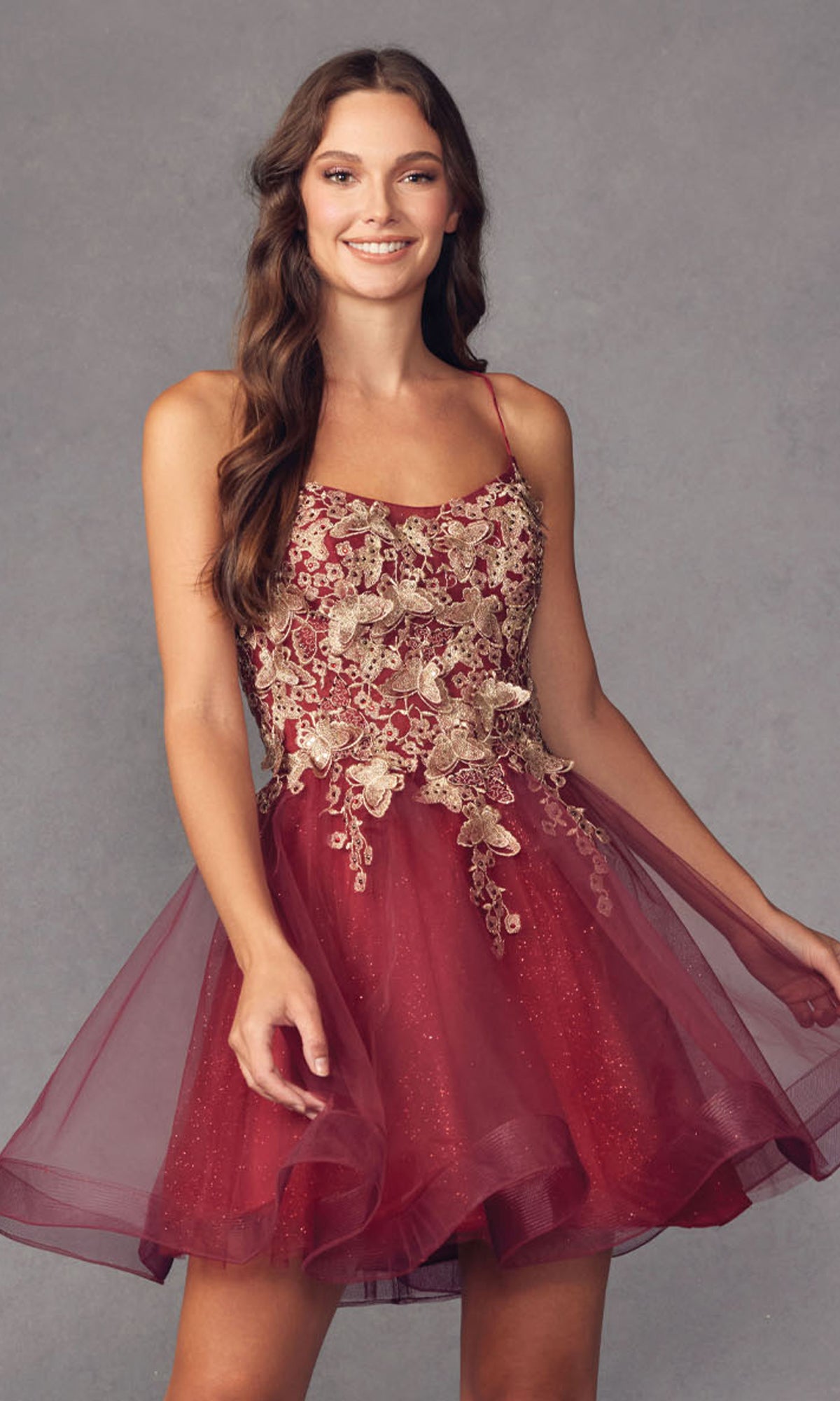A woman in the Short A-Line Butterfly Homecoming Dress 902, featuring a sleeveless design with gold embroidery and a tulle skirt, stands against a plain gray background.