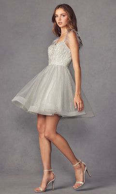 A woman wearing the Short Babydoll Homecoming Dress with Feathers 881 and silver high-heeled sandals stands against a plain gray background.