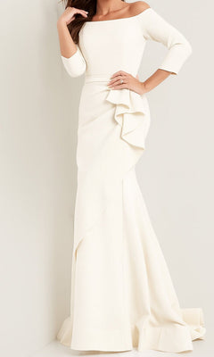 A woman stands against a light-colored wall wearing the Jovani Mother-of-the-Bride Long Formal Dress 00446 in ivory, featuring an off-shoulder neckline, long sleeves, and a floor-length skirt with ruffle detailing.
