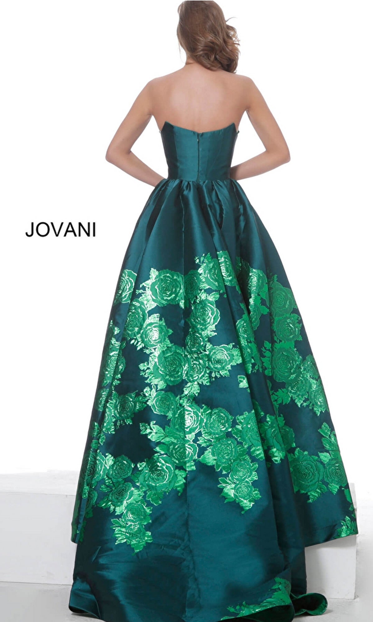 A woman faces away wearing the Jovani Strapless Floral Long Prom Ball Gown 02038—a floor-length teal gown with shiny green floral patterns. 