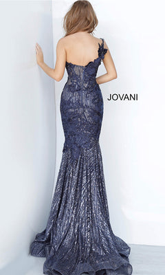 A woman in a navy blue, one-shoulder long glitter prom dress with floral embellishments stands by a white wall. The brand name “Jovani” highlights the elegant Jovani One-Shoulder Glitter Long Prom Dress 02445 beside her.