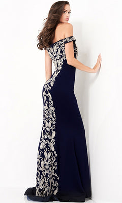 A woman stands facing a white wall, looking over her shoulder and touching the wall, wearing the Jovani Embroidered Off-Shoulder Prom Dress 02576 in navy blue with silver embroidered patterns.