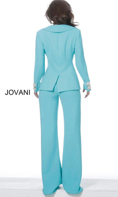 A person wearing the Jovani 02637 Long Jumpsuit in light blue with decorative cuffs stands with their back to the camera against a plain white background. The word “JOVANI” appears on the left side.