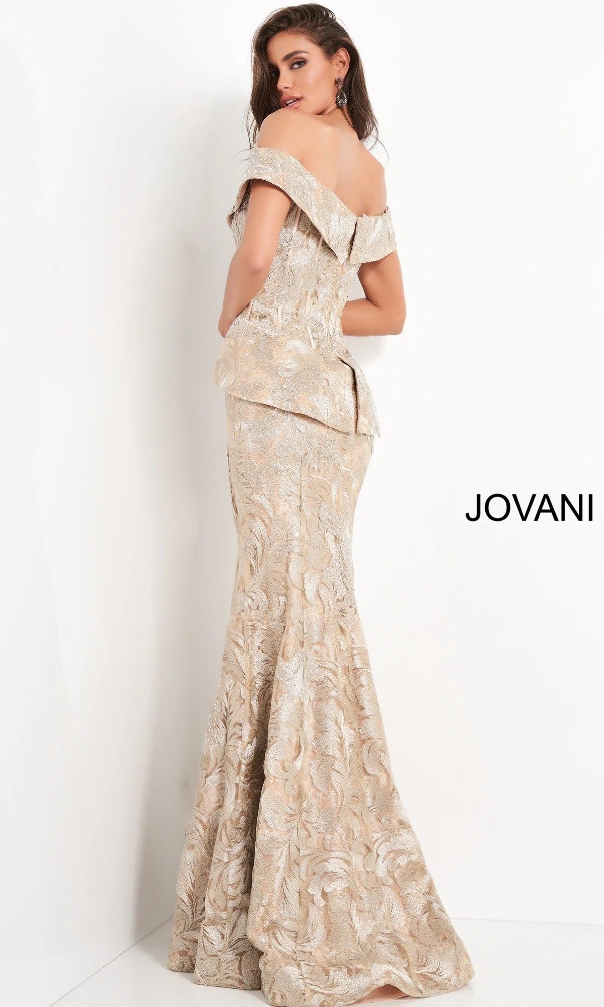 A woman, seen from behind, is wearing the Jovani 02762 long formal dress—a fitted, off-shoulder champagne mermaid evening gown featuring floral patterns and a floor-length silhouette. The word “JOVANI” appears on the right side.