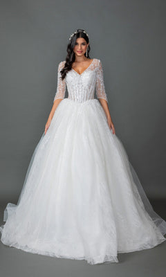A woman wearing the Long Wedding Dress 0323 by Dancing Queen in off white, featuring a tulle ball gown silhouette with a lace-embellished bodice, sheer beaded sleeves, and a full tulle skirt, stands against a plain gray background.