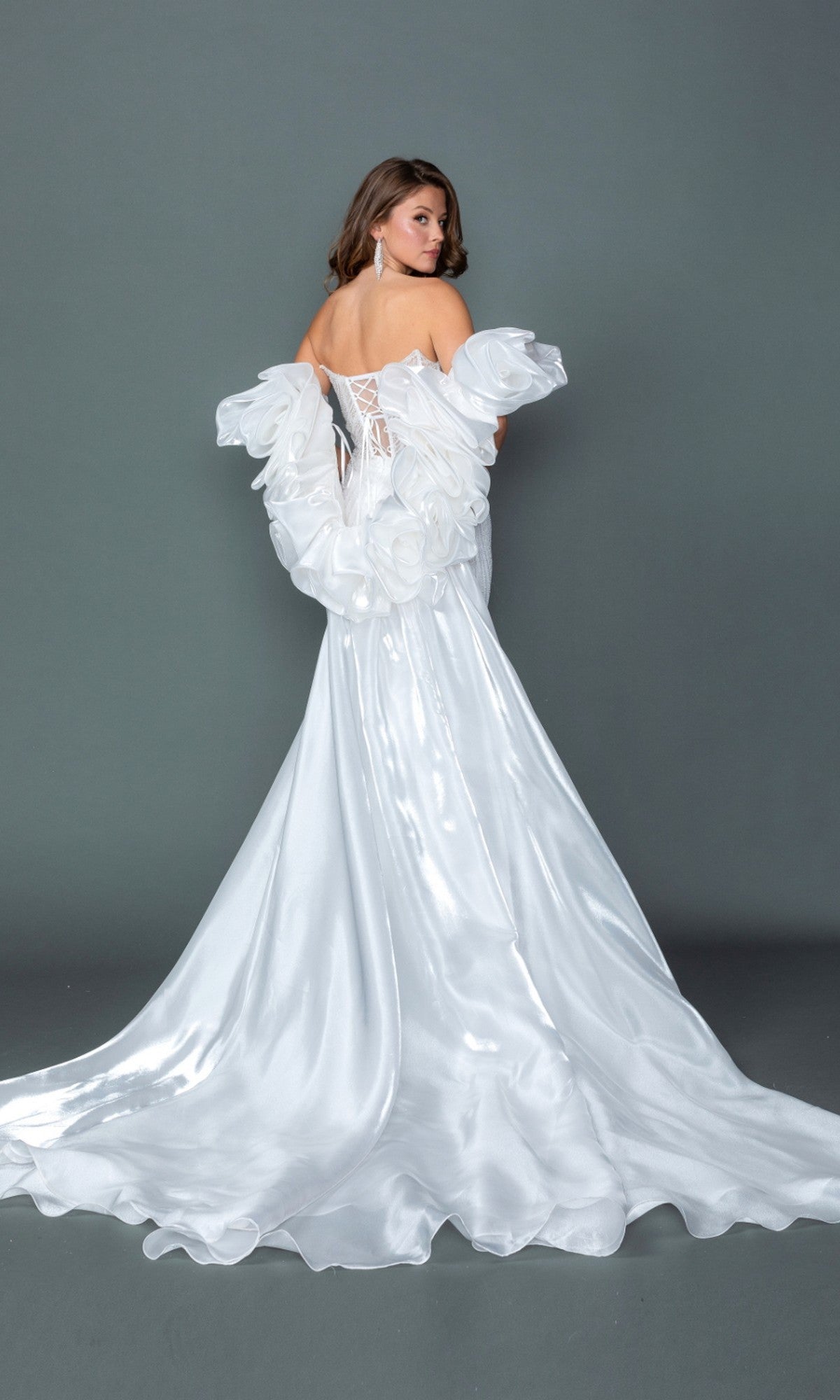 A woman is seen from behind, standing against a plain gray background, wearing the Dancing Queen 0328 Long Wedding Dress—a white satin bridal gown with an off-shoulder design, large ruffles, a strapless corset bodice, and a lace-up back.