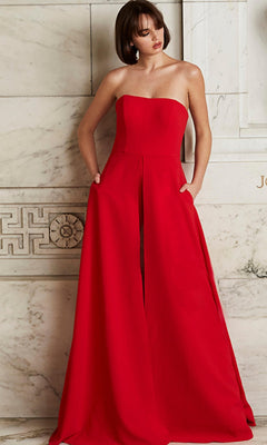 Woman wearing the Jovani Strapless Wide-Leg Formal Jumpsuit 03529 in red, featuring a strapless neckline, floor-length wide legs with a front slit, and pockets, stands against a marble wall.