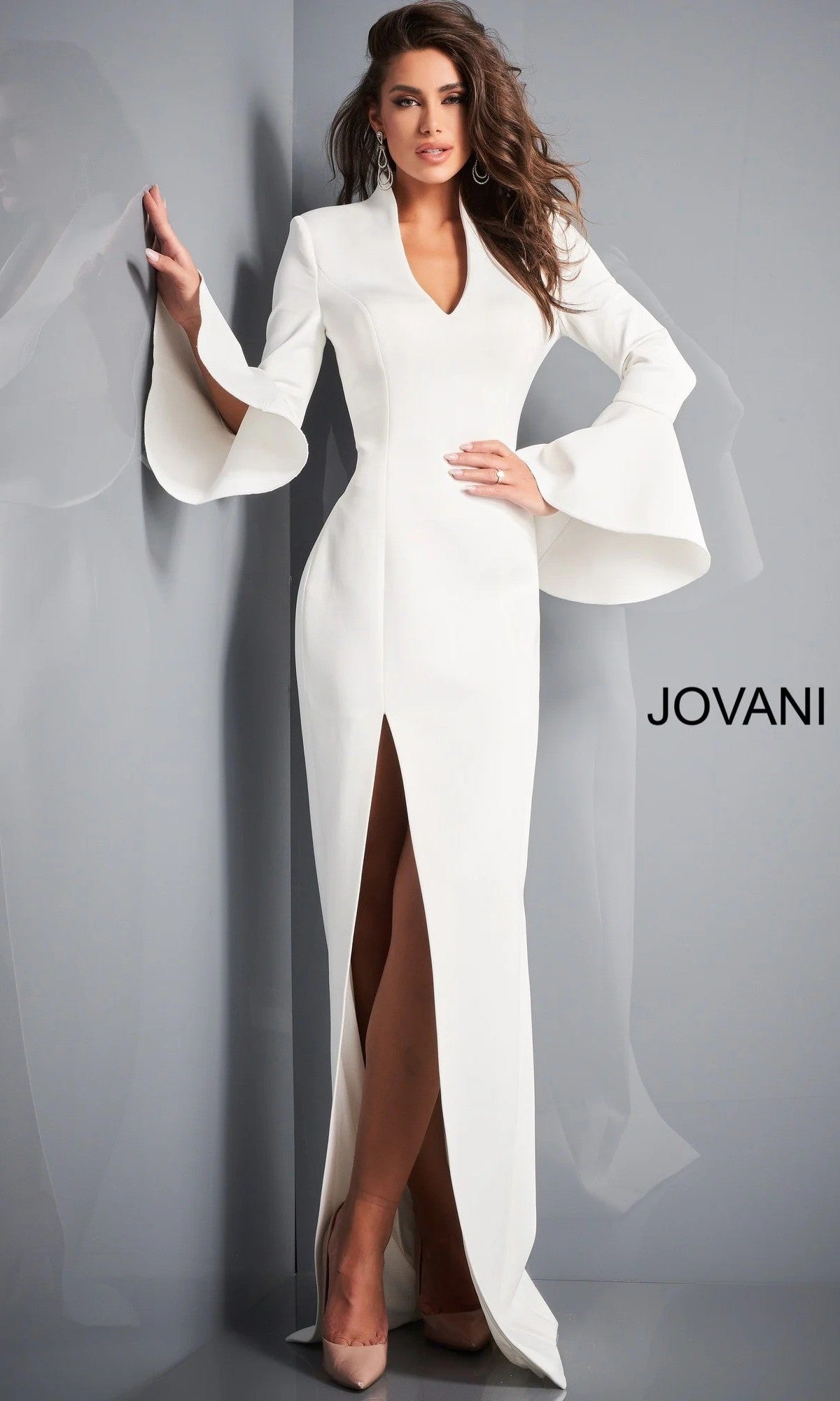 A woman wearing the Jovani 04240 Long Formal Dress, featuring flared bell sleeves and a front slit, stands against a gray wall with “JOVANI” displayed on the right side.