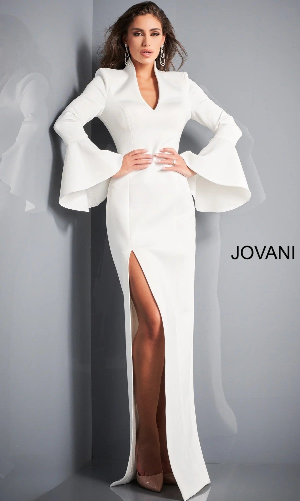 A woman wearing the Jovani 04240 long formal dress in white, featuring flared sleeves and a front slit, stands against a gray wall. The word “JOVANI” is displayed on the right side of the image.