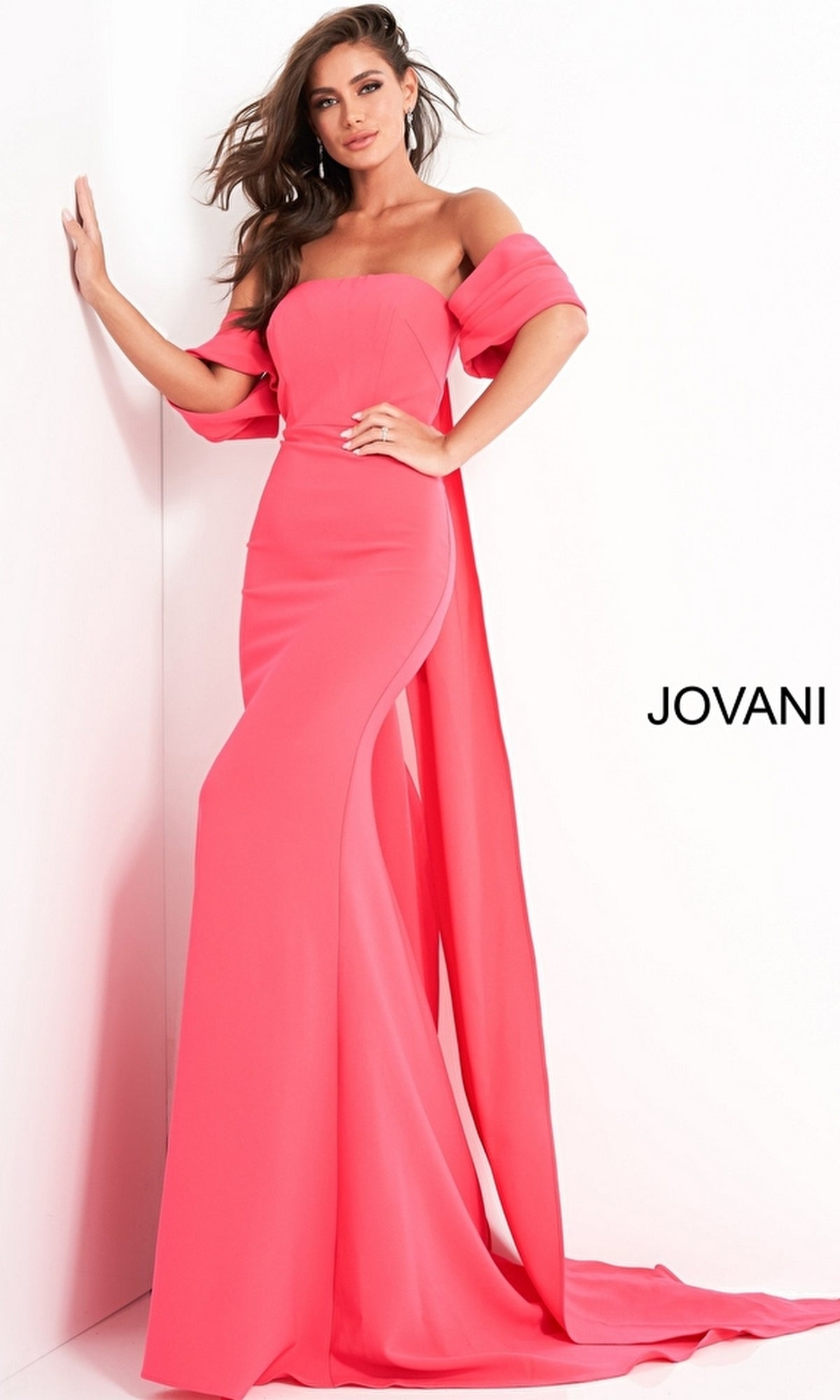 A woman models the Long Prom Dress by Jovani 04350—a strapless, floor-length bright pink gown with a matching draped shawl—standing near a white wall featuring the 